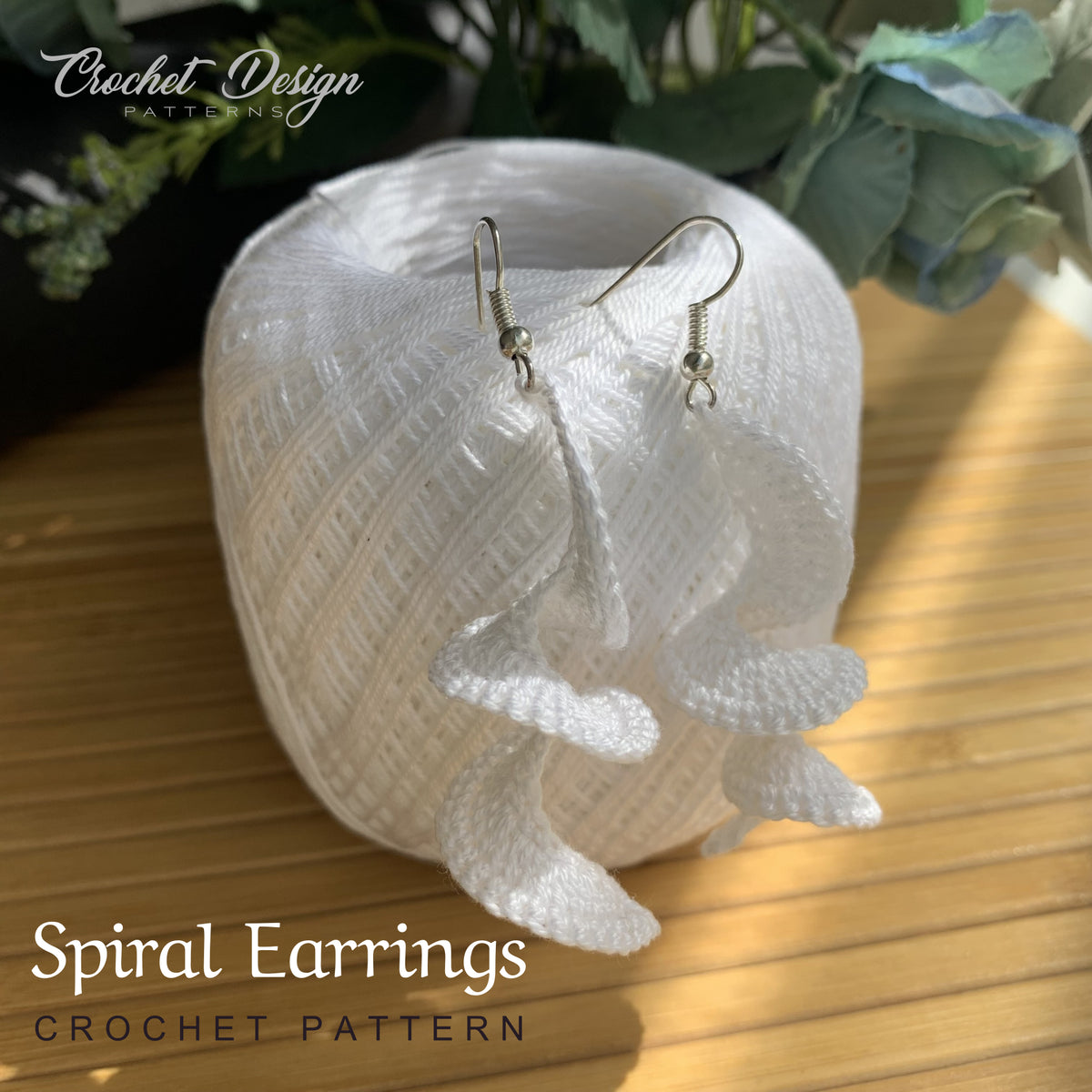 Crochet spiral earrings displayed on white yarn thread skein used for the pattern