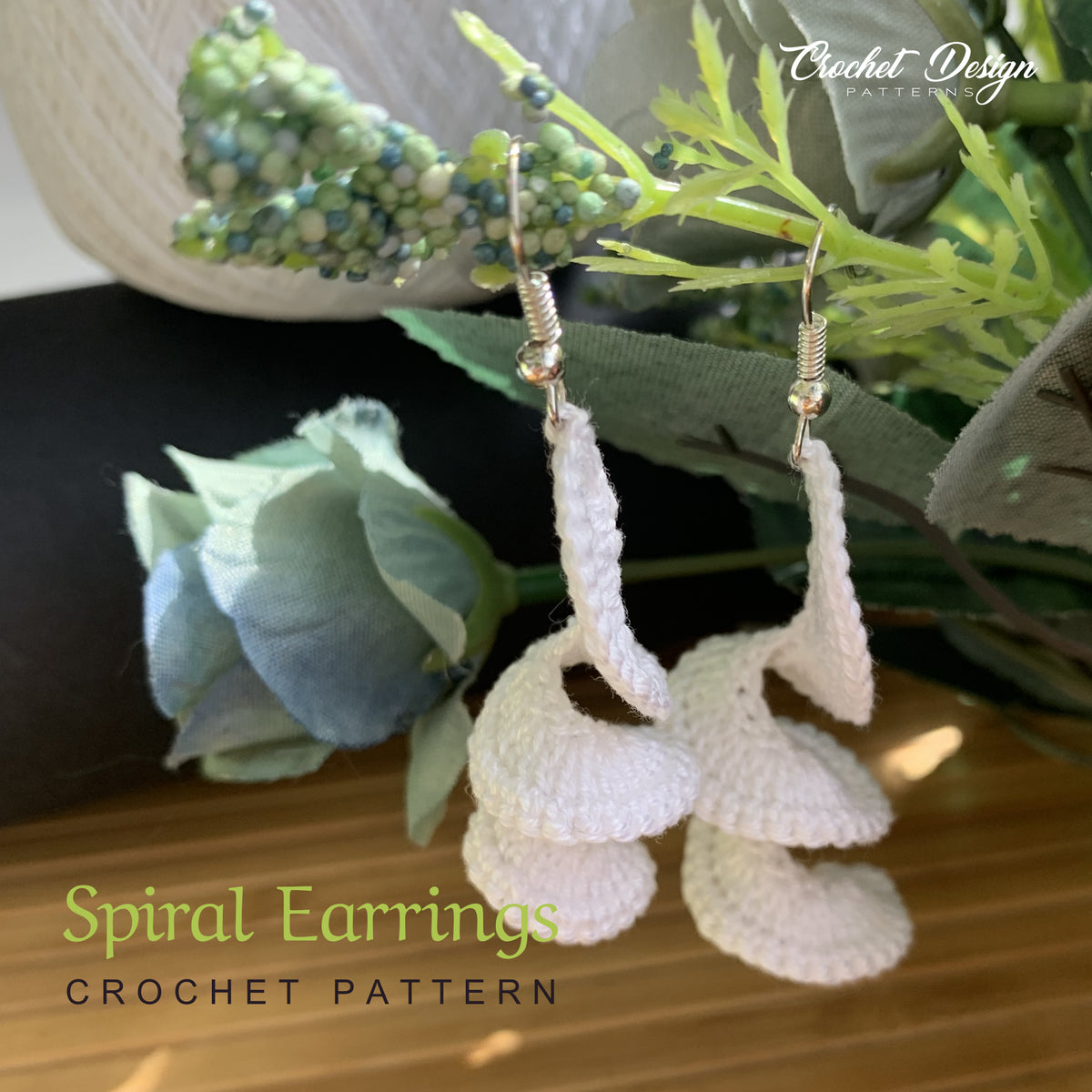 White crochet spiral earrings hanging, styled with greenery
